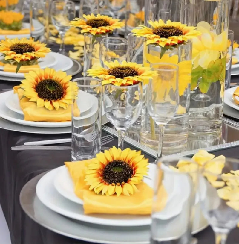 Yellow artificial sunflower heads arranged in glass vases on a table setting.