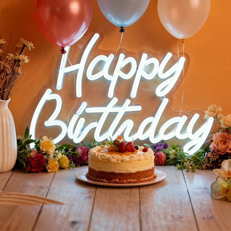 A glowing neon sign spelling out Happy Birthday with balloons and floral arrangements in the background.