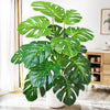 A vibrant artificial monstera plant with large green silk leaves displayed indoors.