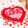 A heart shape made of red and pink silk rose petals scattered on a white surface.