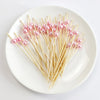 A plate holds numerous pearl-tipped bamboo cocktail picks with a white pearl finish.