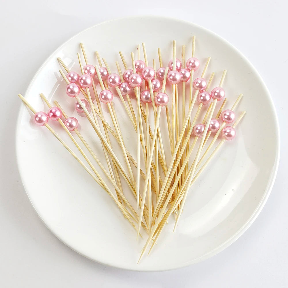 A plate holds numerous pearl-tipped bamboo cocktail picks with a white pearl finish.