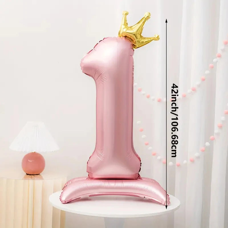 A pink foil number balloon shaped like the number one with a gold crown on top