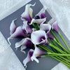 A bouquet of five white calla lily stems with purple accents arranged on a gray card.
