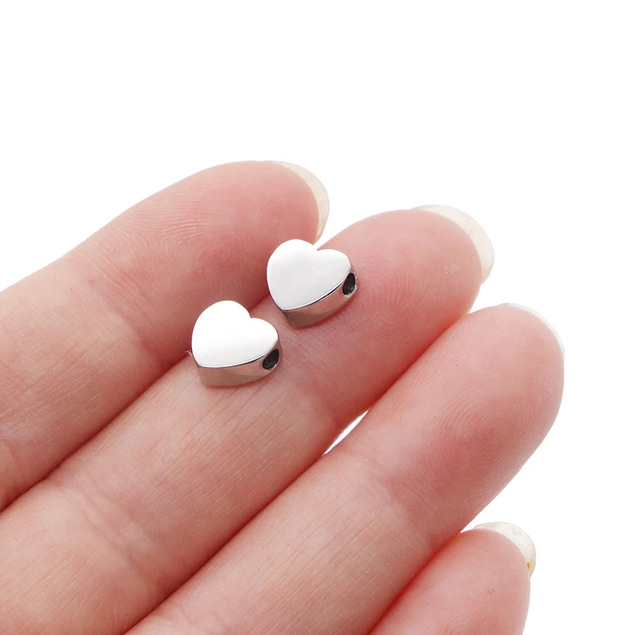 Two silver heart-shaped stainless steel bead charms resting on a person's hand.