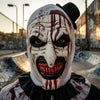 A close-up of a horror clown mask costume with white face paint, red blood splatters, and a black top hat.