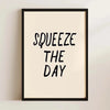 A framed canvas print with black text that reads SQUEEZE THE DAY on a light beige background.