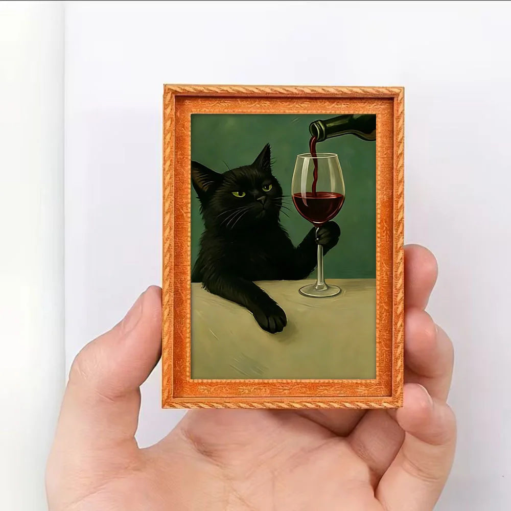A framed picture of a black cat drinking red wine, held by a hand.