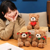 A plush toy of a brown bear with a red heart on its chest sits next to a woman.