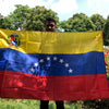 A person holds a large Venezuelan flag banner outdoors under a bright sky.