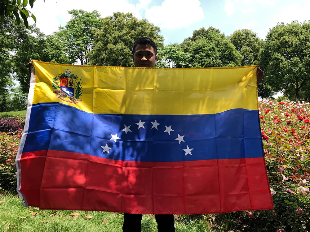 A person holds a large Venezuelan flag banner outdoors under a bright sky.