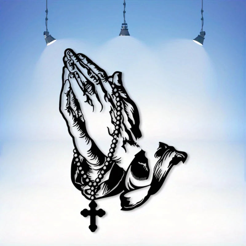 Black silhouette of praying hands with a cross, displayed against a light blue background under hanging lights.