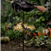 A black witch wind rotator garden decor featuring a dark fabric and a broomstick on a metal stand.