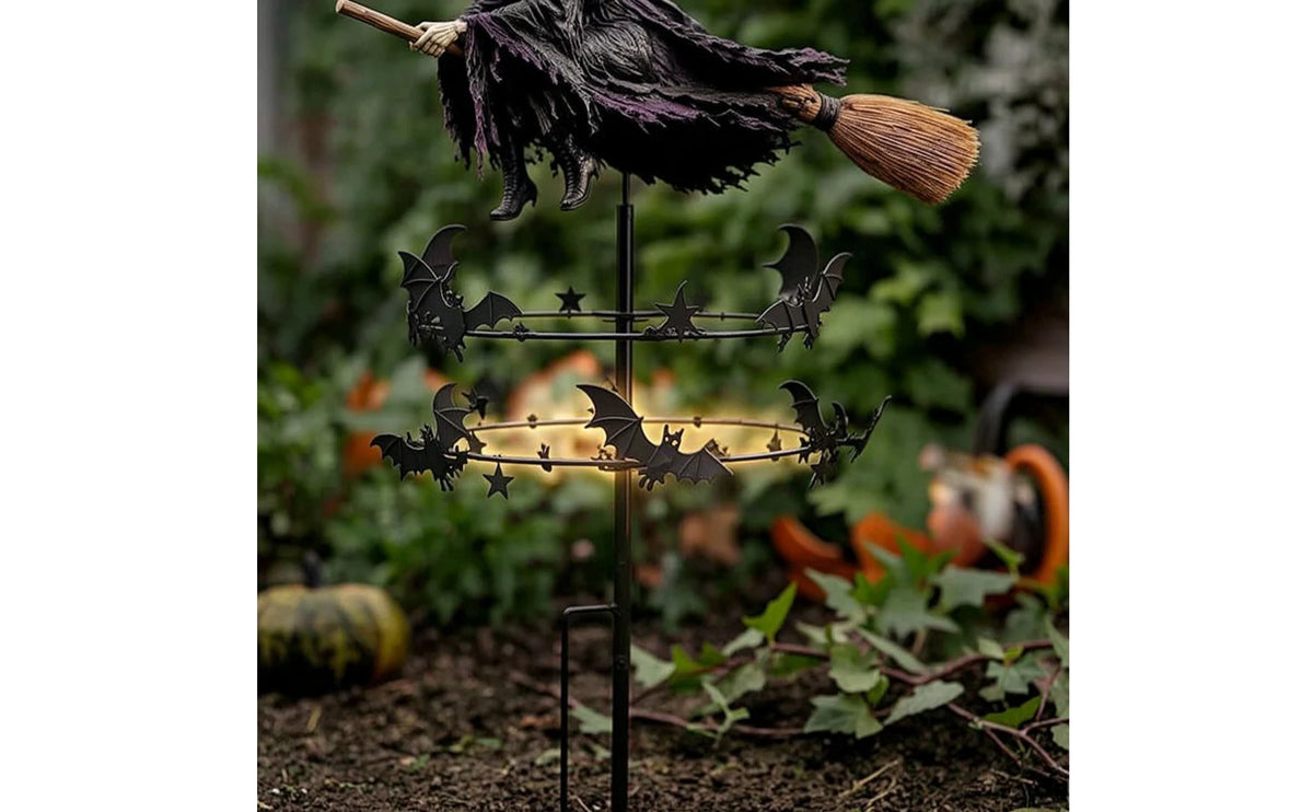A black witch wind rotator garden decor featuring a dark fabric and a broomstick on a metal stand.