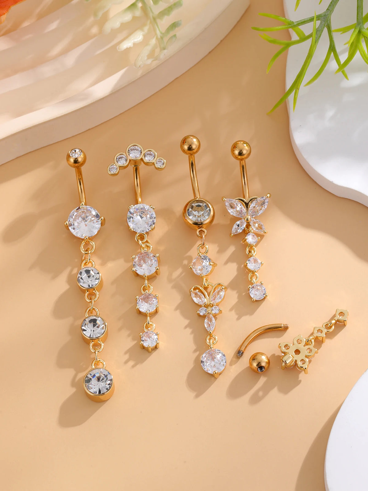 A set of five gold tone butterfly and flower belly rings displayed on a light beige surface.