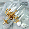 A set of nine white candles in gold holders displayed on sheer fabric with glitter.