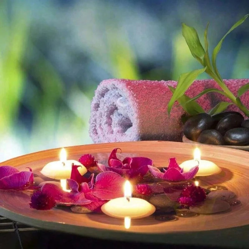 Pink floating candles on a wooden plate surrounded by dark petals and green leaves