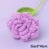 A handmade purple crochet rose flower with a green leaf on a light purple background.