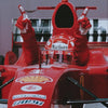 A close-up of a red Formula 1 racing car cockpit with a driver's hands and helmet visible.
