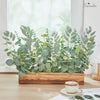 A lush arrangement of mixed artificial eucalyptus leaves in various shades of green displayed in a wooden planter.