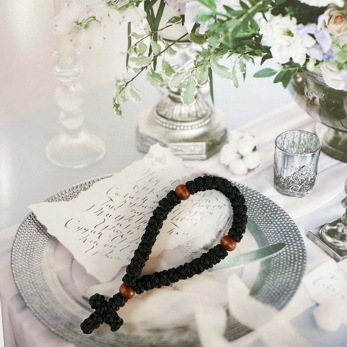 A handmade black 33-knot Orthodox prayer rope with a wooden cross charm resting on a silver plate.