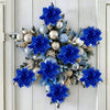 A festive arrangement of blue glitter artificial poinsettia flowers and silver spherical ornaments on a white door.