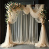 A sheer beige tulle fabric draped as a wedding backdrop with floral accents.