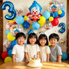 Four children posing in front of a wall decorated with large blue and yellow balloons and a cake.