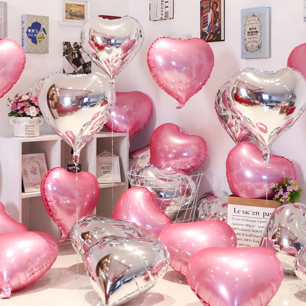 Eine Sammlung rosa und silberne herzförmige Folienballons auf einem weißen Regal