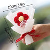 A hand holds a bouquet of handmade red and yellow crochet flowers wrapped in white paper.