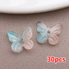 Colección de cuentas de mariposa de vidrio azul claro y rosa translúcido esparcidas sobre una superficie gris texturizada.