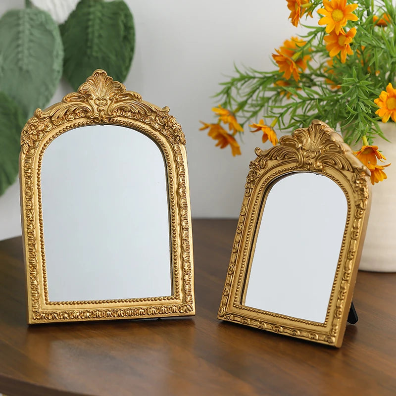 A pair of ornate gold-framed vintage arched vanity mirrors resting on a dark wooden surface.