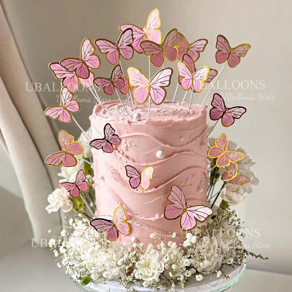 A pink buttercream cake decorated with eleven edible butterfly toppers in shades of gold, pink, and purple flowers.