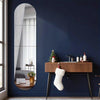 A dark blue wall features a tall arched mirror reflecting white curtains and a wooden console table with decorative items.