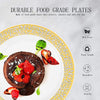 A white plate with a gold rim holds a dark chocolate pancake topped with fresh strawberries and a green leaf.