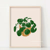 Botanical philodendron canvas wall art featuring a green plant in an orange pot framed in light wood.