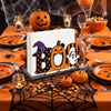A wooden tissue dispenser with a Boo pumpkin design displayed on an orange tablecloth surrounded by Halloween decor.