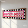 A framed canvas print featuring the text Kitchen Disco in bright pink and red on a black and white checkered background.