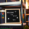 A wooden message board with white text and icons welcoming to sky inside a glass frame.