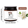 A dark glass jar candle labeled jasmine with a design featuring a couple and flowers.