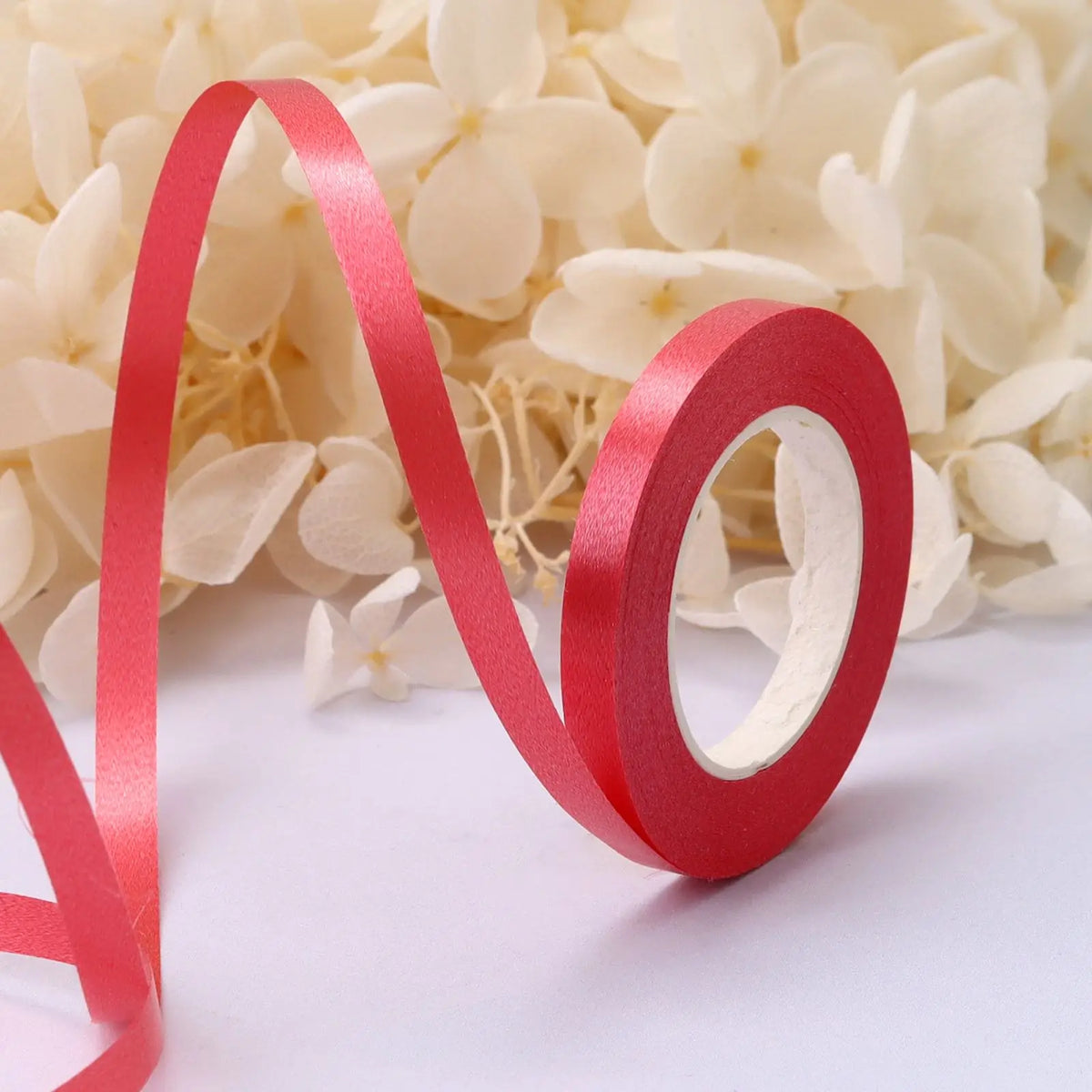 A red satin ribbon scroll forming the letter 'V' and 'O' is placed on a white background surrounded by white flowers.