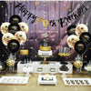 A black and gold glitter birthday banner strung across a backdrop with balloons and cake decorations.