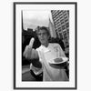 Black and white photograph of a man making a finger sign in front of a city skyline.