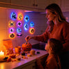 A woman and a child are decorating a kitchen counter with Halloween LED night lights and pumpkin decorations.