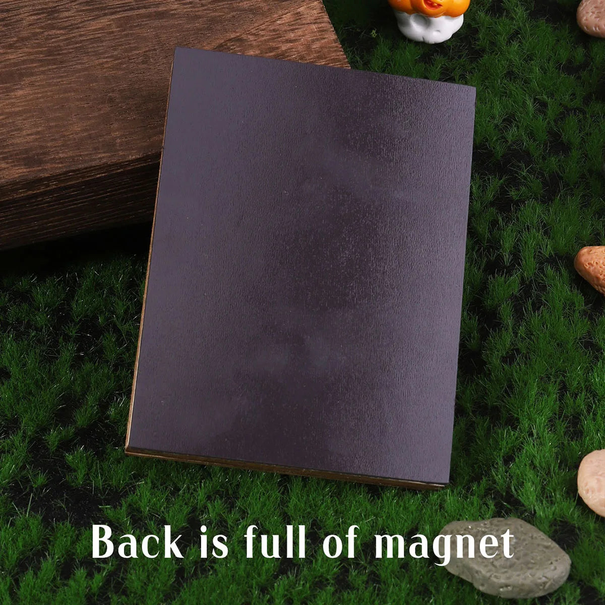 A dark rectangular magnet with a gold edge is placed on green moss next to a wooden block.
