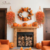 A decorative wreath of autumn leaves and pumpkins hangs on a white wall with orange floral garlands.
