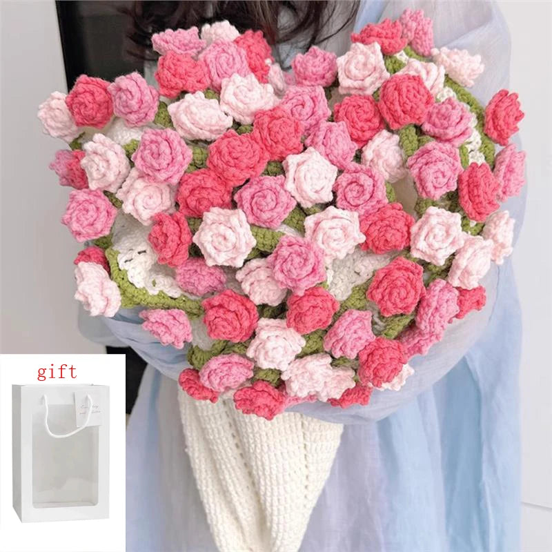 A handmade rose bouquet blanket gift made of pink and red yarn is held against a light blue fabric.
