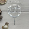 Silver acrylic cake topper with happy birthday text on a stick set against a light wooden background