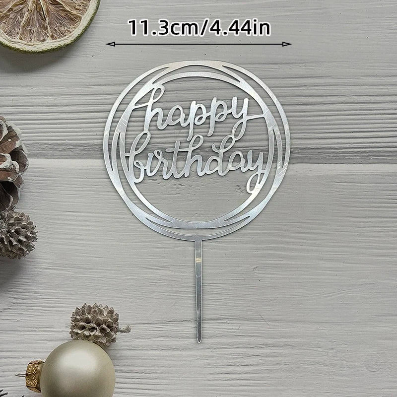 Silver acrylic cake topper with happy birthday text on a stick set against a light wooden background