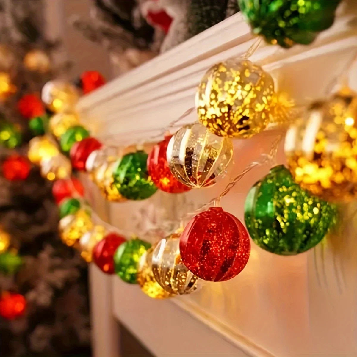 A string of festive gold and red LED fairy lights decorated with shiny spherical ornaments on a white mantelpiece.